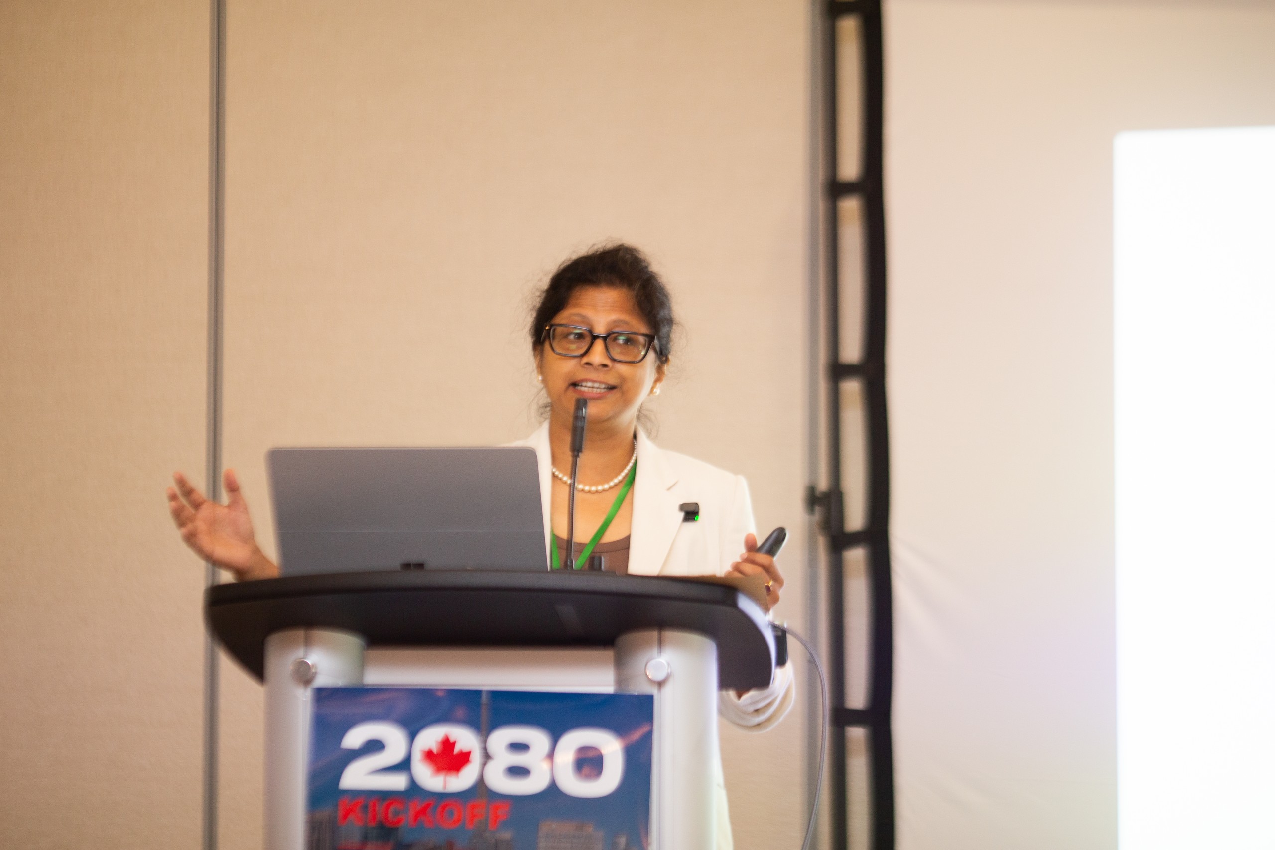 Dr Sudarshana Bhattacharya speaking at the podium in a white blazer.