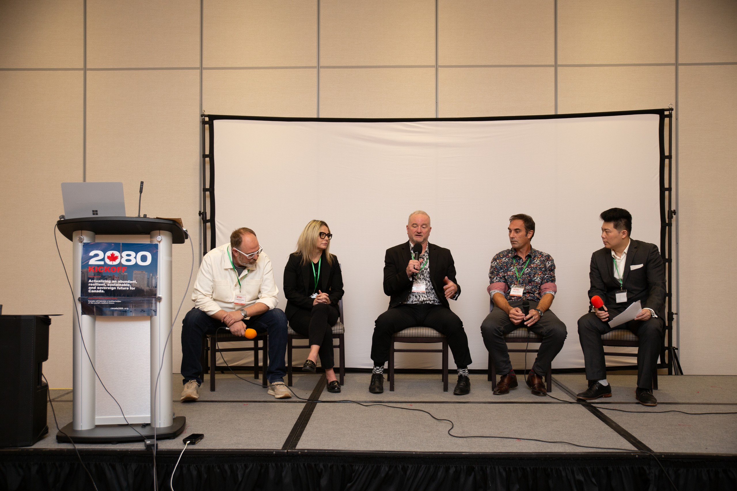 Five people seated on stage for Panel 2. Francis Wang is at the right with a red microphone.