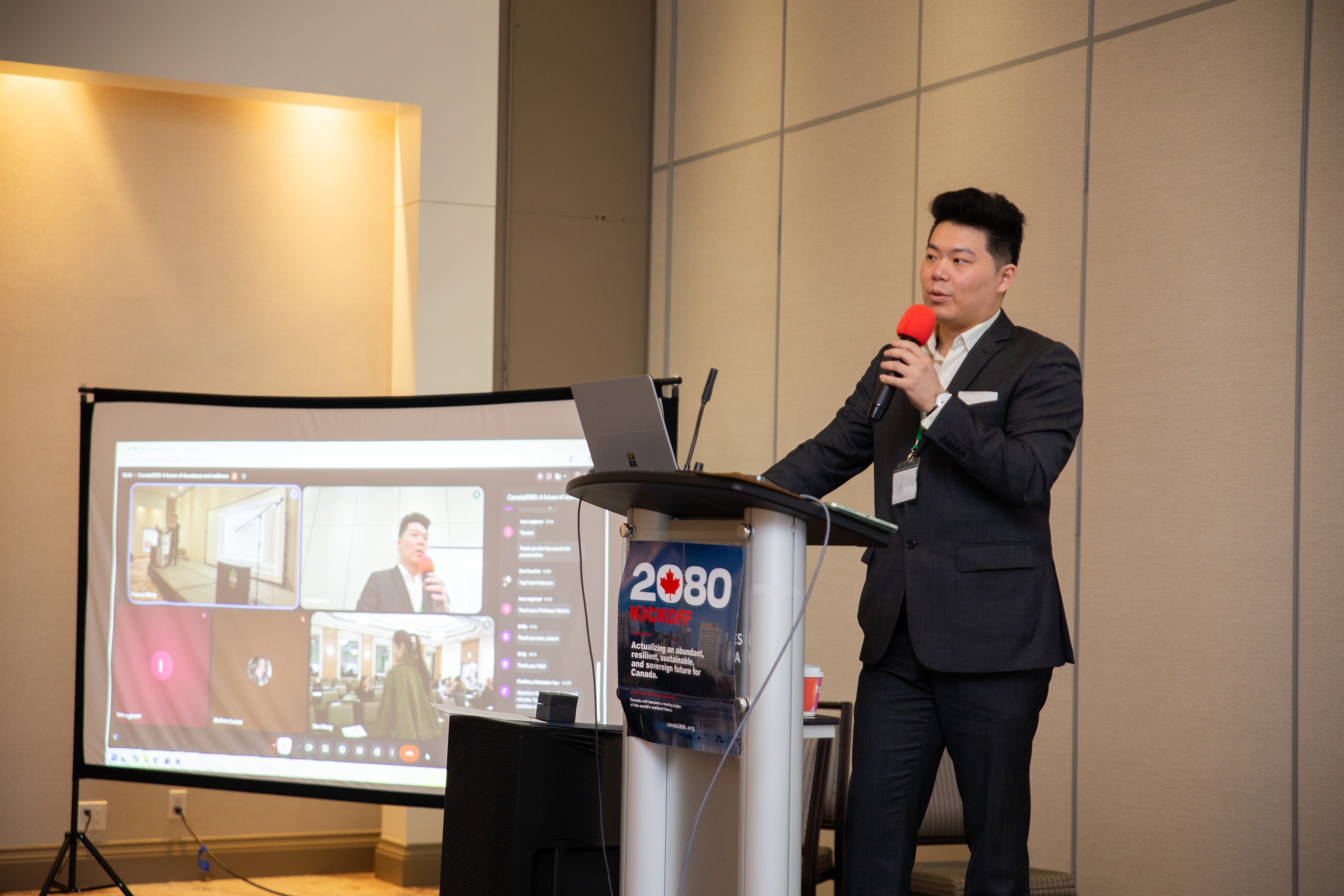 Francis Wang at the podium with a red microphone, closing the kickoff.
